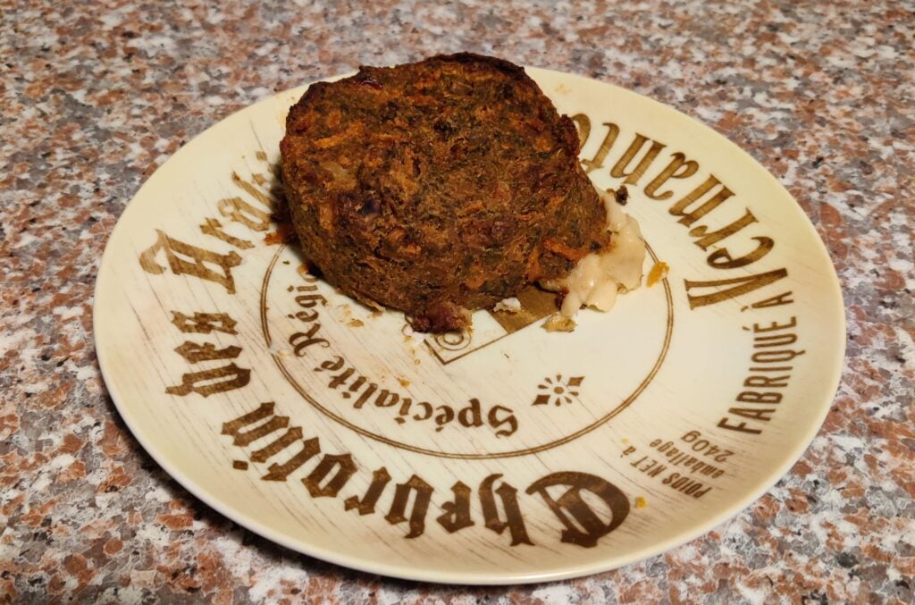 A cooked vegan nut roast served on a plate, it looks like a dry brown lump with some white stuff oozing out.